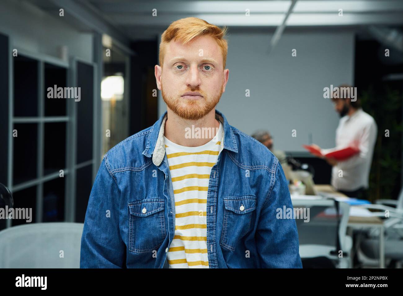 Young red-haired programmer or businessman in modern office looking seriously at camera. Stock Photo