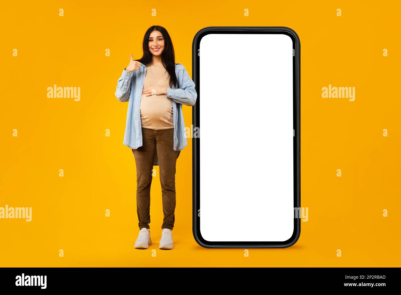 Smiling expectant woman standing near big cellphone with blank screen ...