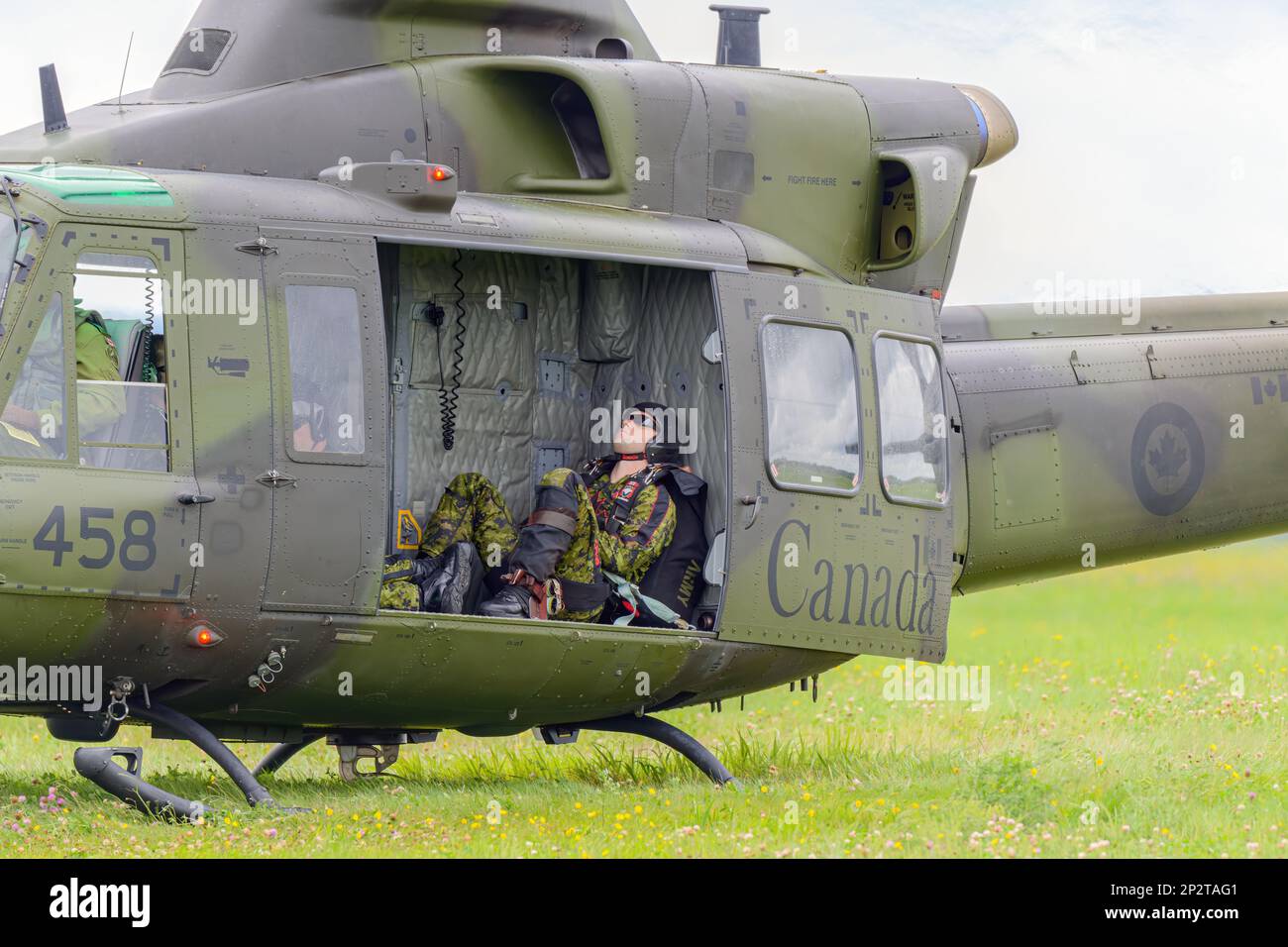 Moncton, NB, Canada - August 23, 2014: Soldier takes a nap in a Griffon helicopter. The helicopter is in grass with side door open. Stock Photo