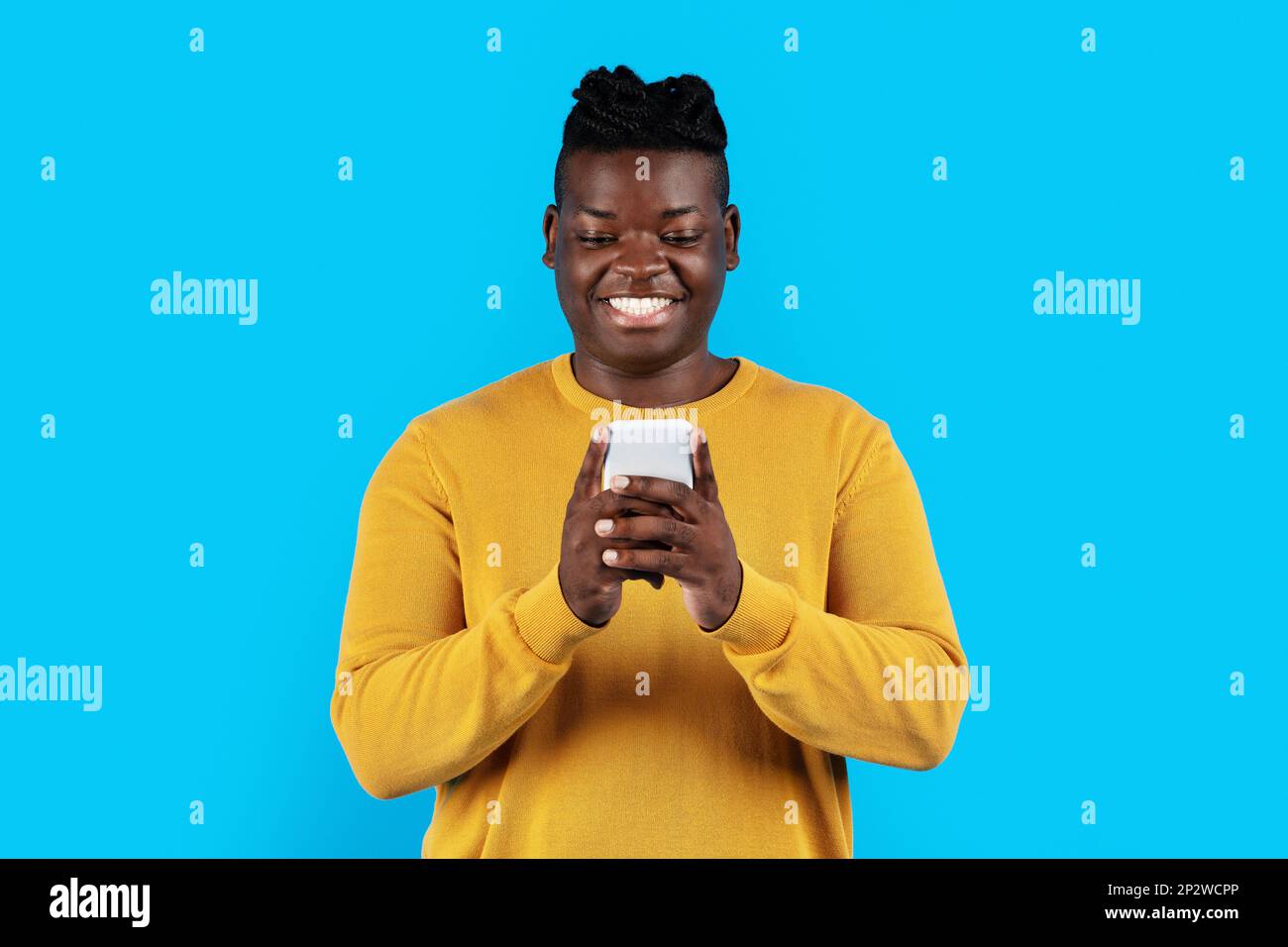 Young Black Man Using Modern Smartphone While Standing Over Blue Studio Background Stock Photo