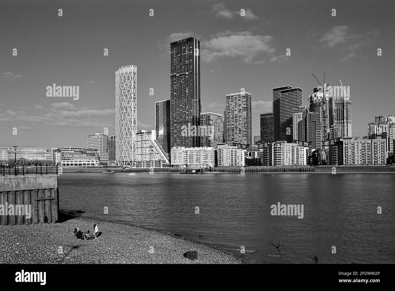 The south bank of the River Thames opposite Canary Wharf, London UK, with people on the beach, in monochrome Stock Photo