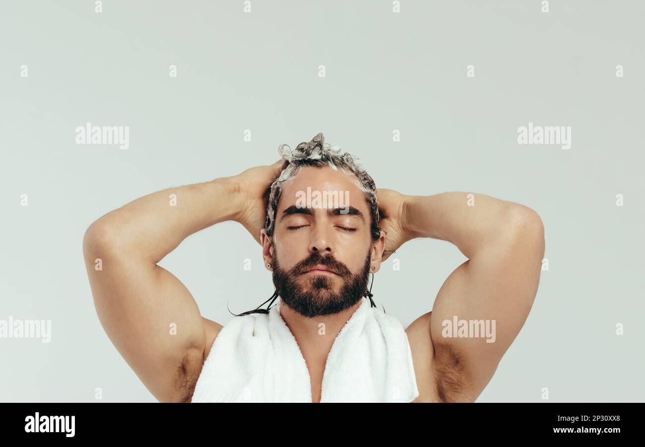 Man applies shampoo to his hair, using his fingertips to gently massage it into his scalp. Young man getting into his hair care routine with a good sh Stock Photo