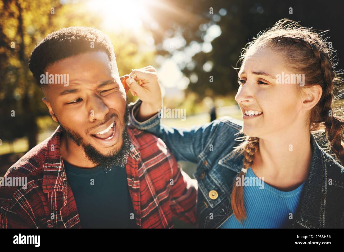 Playful, park and a girl pulling the ear of her boyfriend outdoor during  summer for love while on a date. Couple, game or nature with a young man  and Stock Photo -