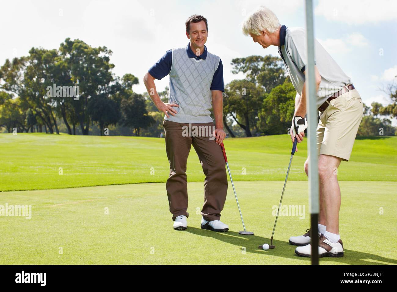 Golfing is a great way to bond. Two men out on the green playing a round of golf together. Stock Photo