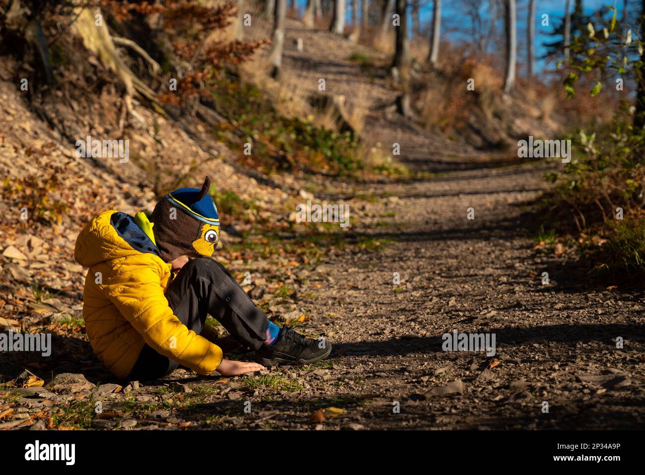 Little kid sitting on the hiking trail in a grumpy mood. Fall season ...