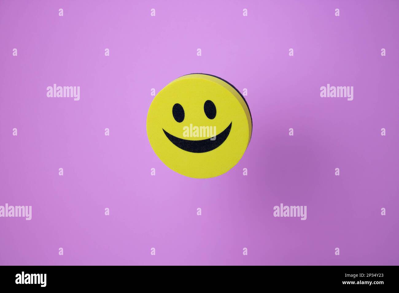 A yellow smiling smiley face and its shadow on a pink background Stock Photo