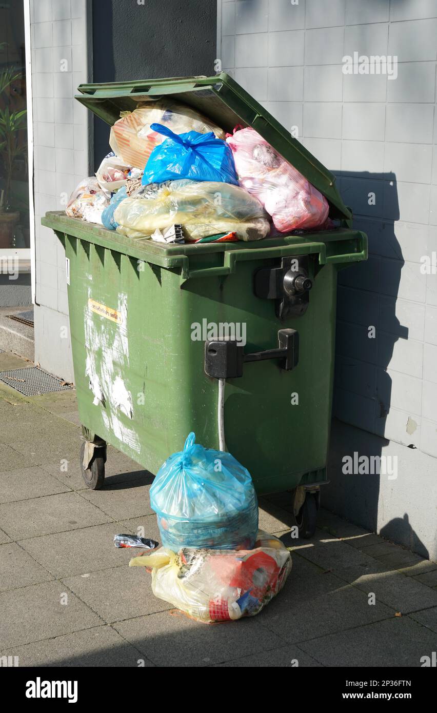 wheeled trash can container overflowing with garbage bags Stock Photo