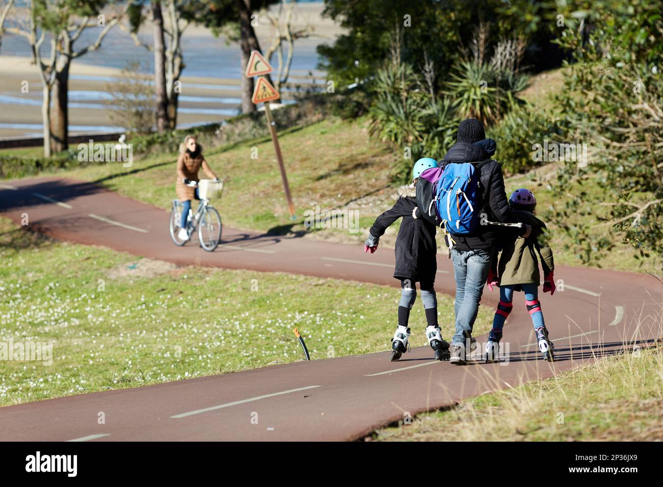 father teaching his daughters to rollerblade on a bike path Stock Photo