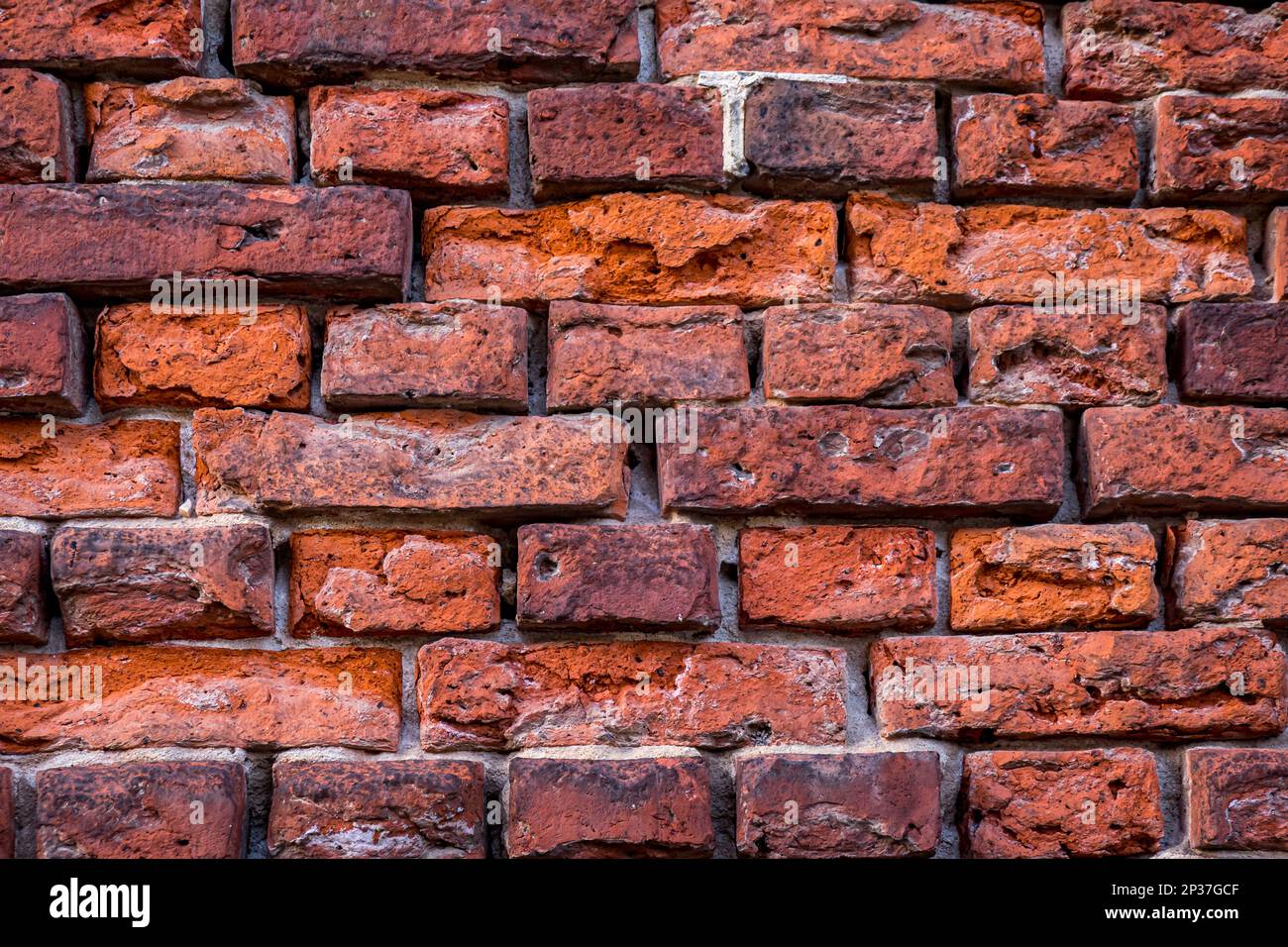 Close-up of a weathered brick wall displays a interplay of varying shades of red, ranging from rusty orange to purple. Stock Photo