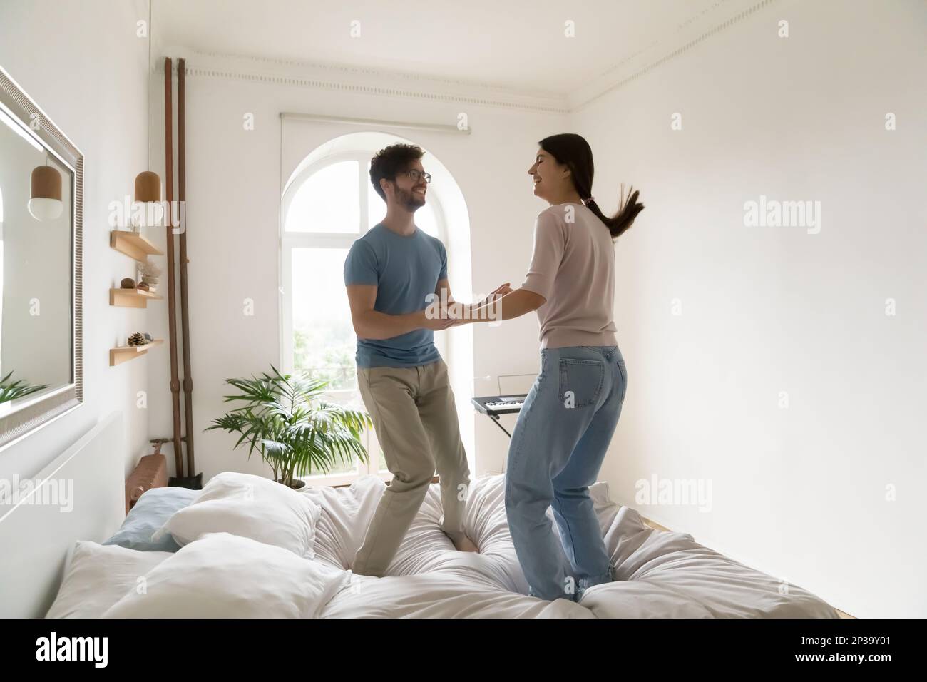 Excited active young couple holding hands, jumping on bed Stock Photo