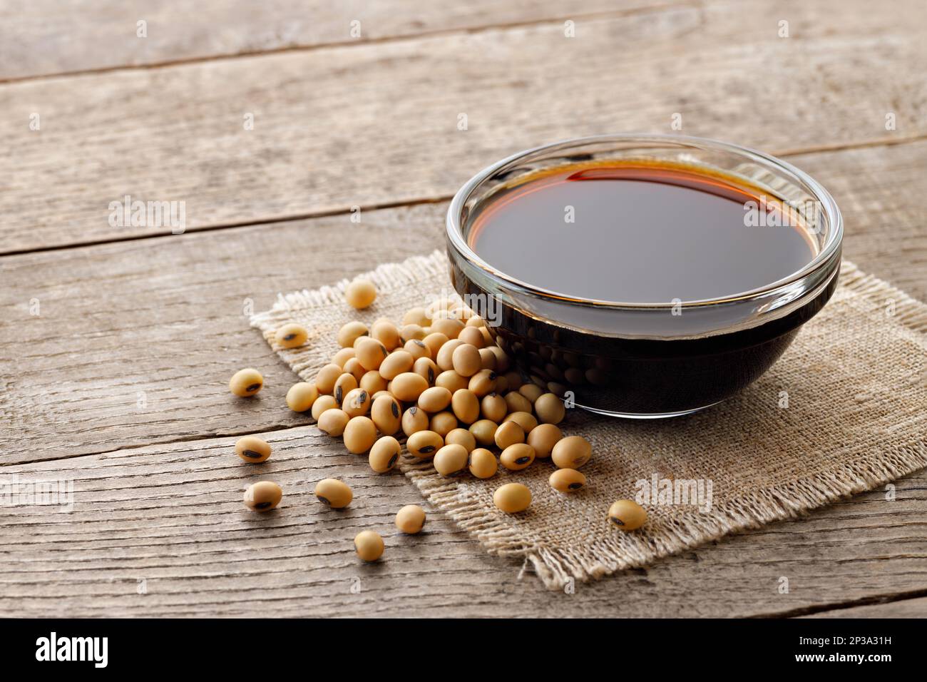 soy sauce in glass bowl with dry soybeans on wooden table Stock Photo