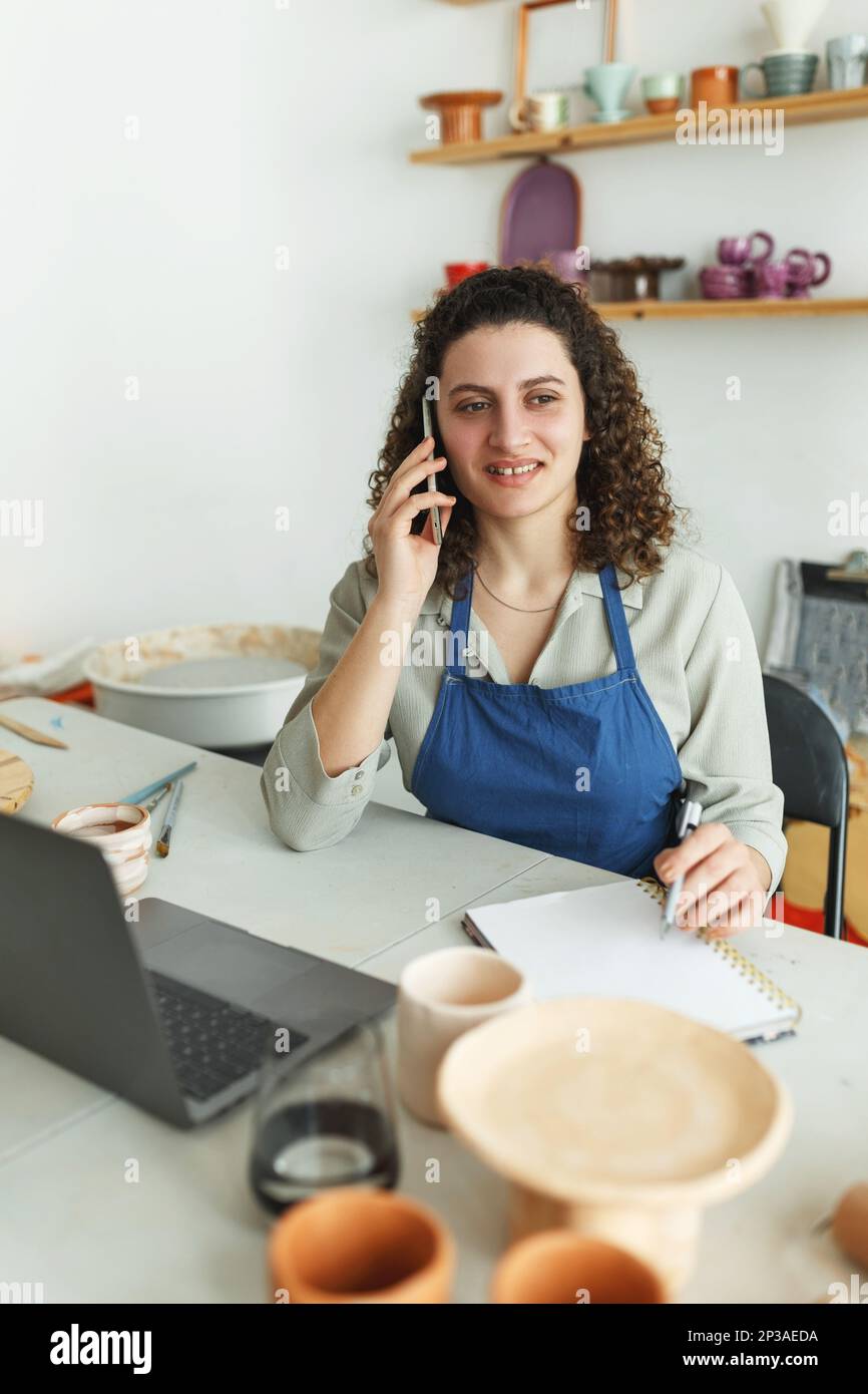 Potter entrepreneur using laptop in workshop, smiling Stock Photo