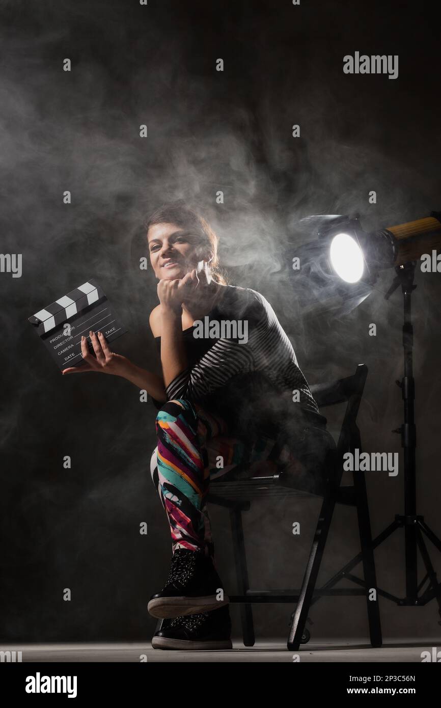 Female movie director. Girl holding clapperboard on set with smoke effects in the air. Stock Photo