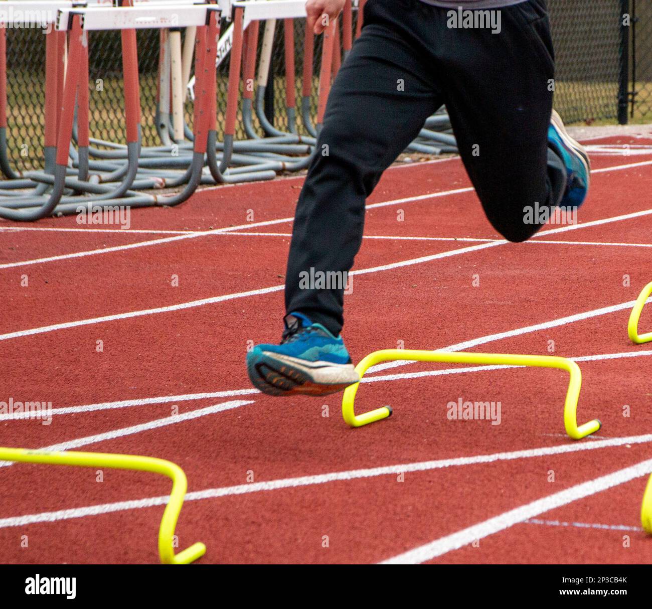 Close up of legs of a runner in the air over yellow mini hurdles