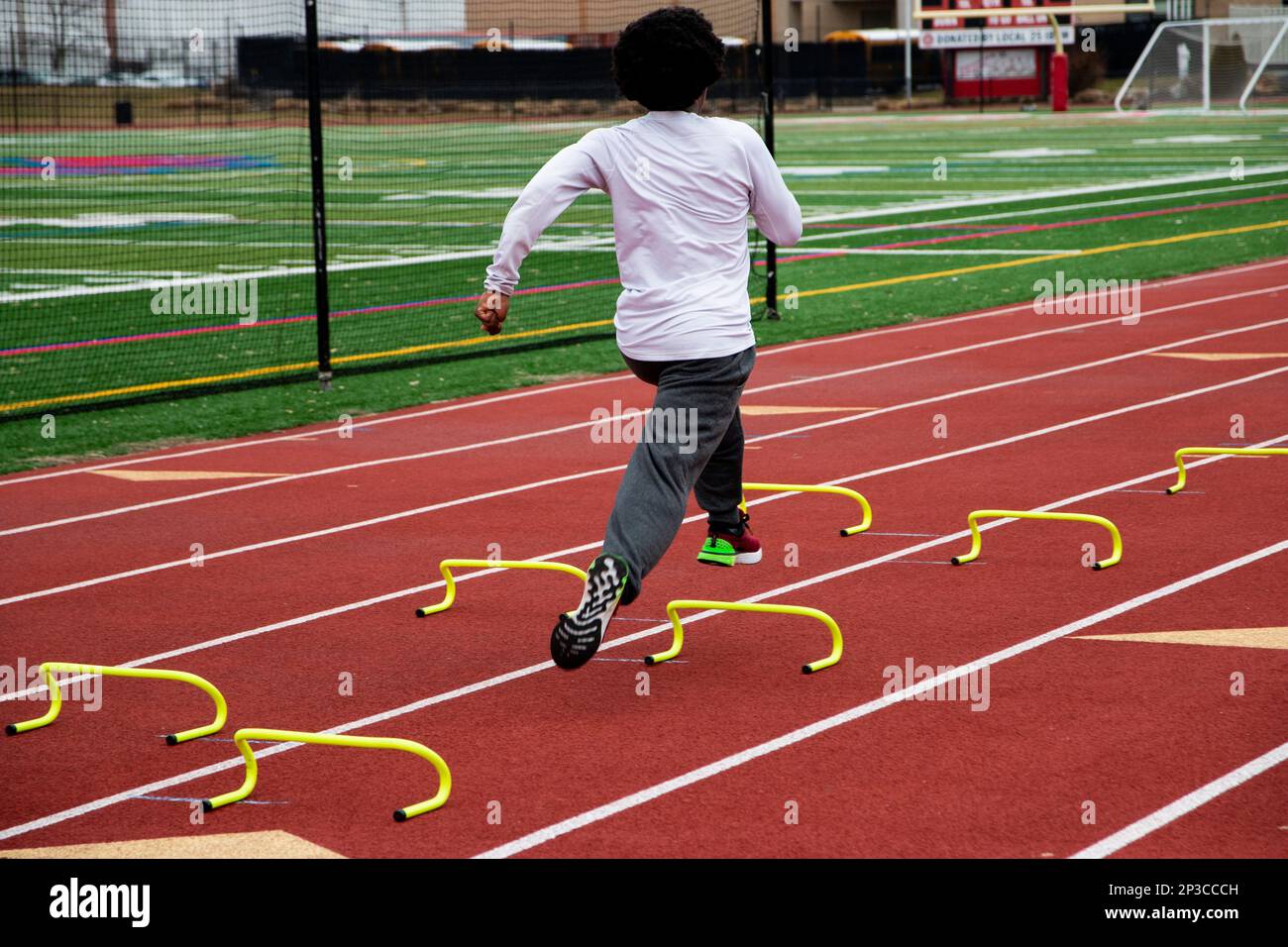 Rear view of a high school boy running the wicket drill on a red track