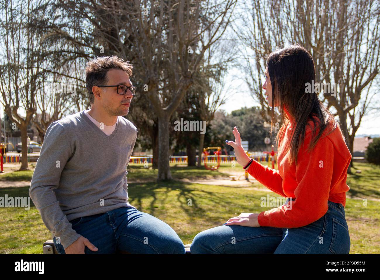 Couple of a mature man and a young woman, chatting and sharing their time, in a garden on a sunny day Stock Photo