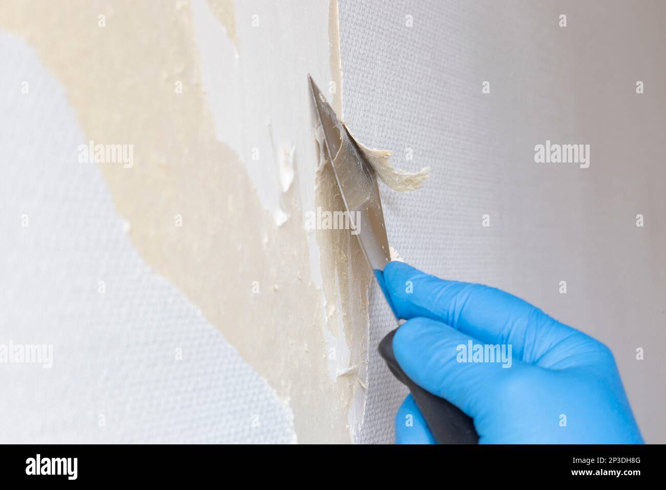Person stripping wallpaper using a scraper hand tool. Do it yourself