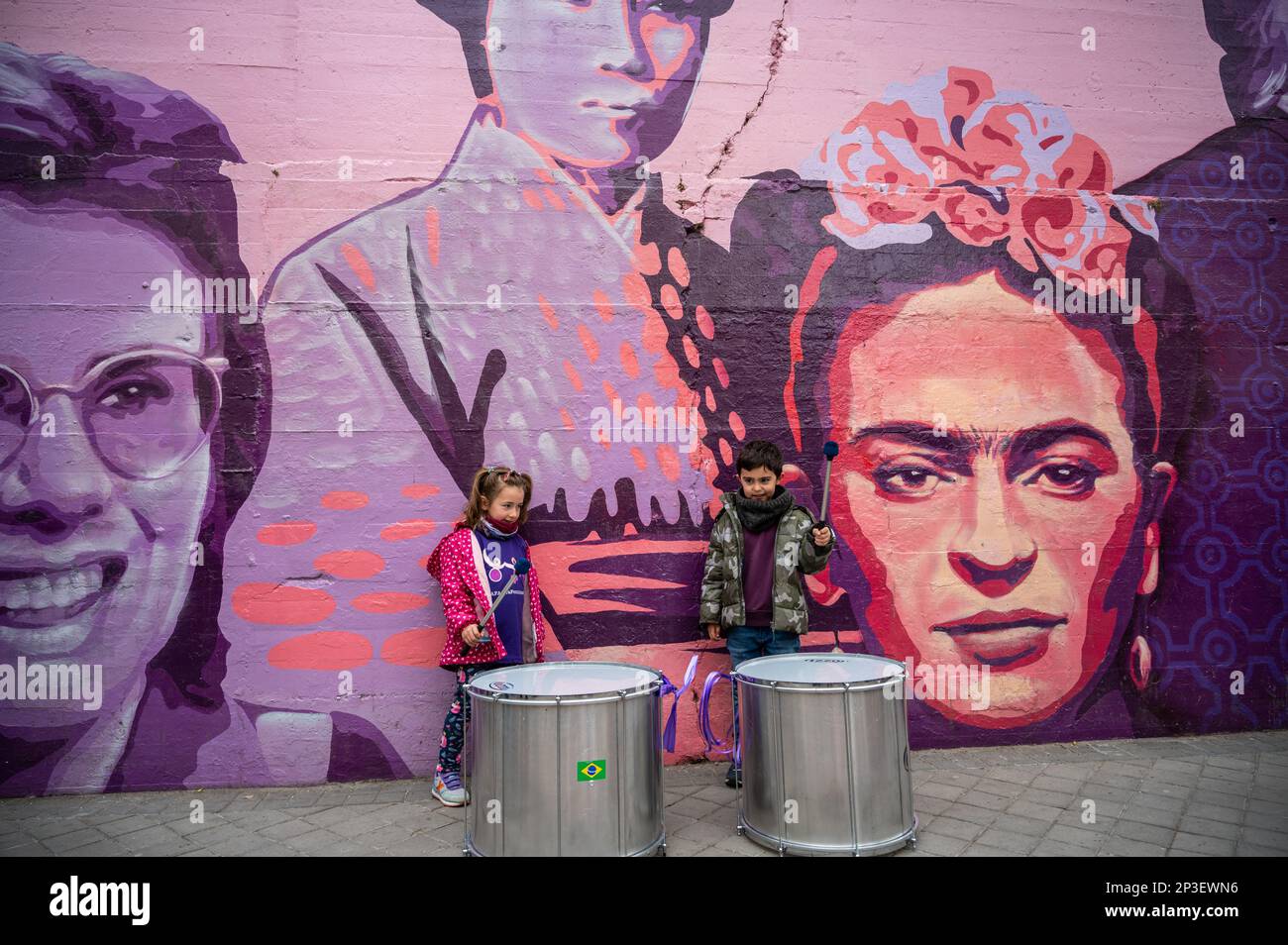 Madrid, Spain. 05th Mar, 2023. Two kids playing drums standing in front of a feminist mural ahead of a human chain performance to denounce violence against women and make visible the feminist struggle. The human chain is part of the activities for International Women's Day. In the mural appear the faces of 15 women who are part of history for their fight in favor of equality such as Angela Davis, Frida Kahlo, Nina Simone, among others. Credit: Marcos del Mazo/Alamy Live News Stock Photo