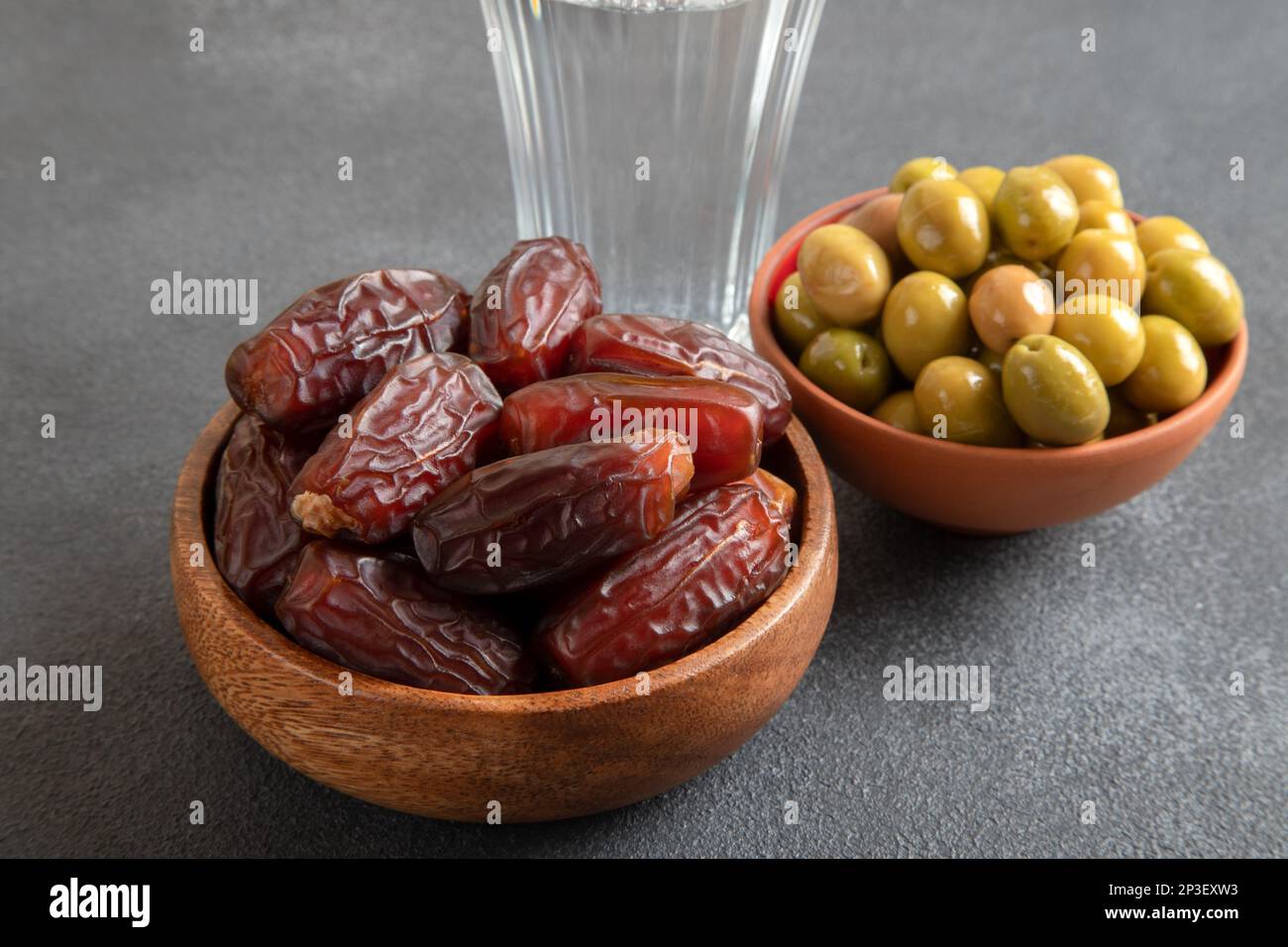 Date fruit, olives and a glass of water on black background Stock Photo