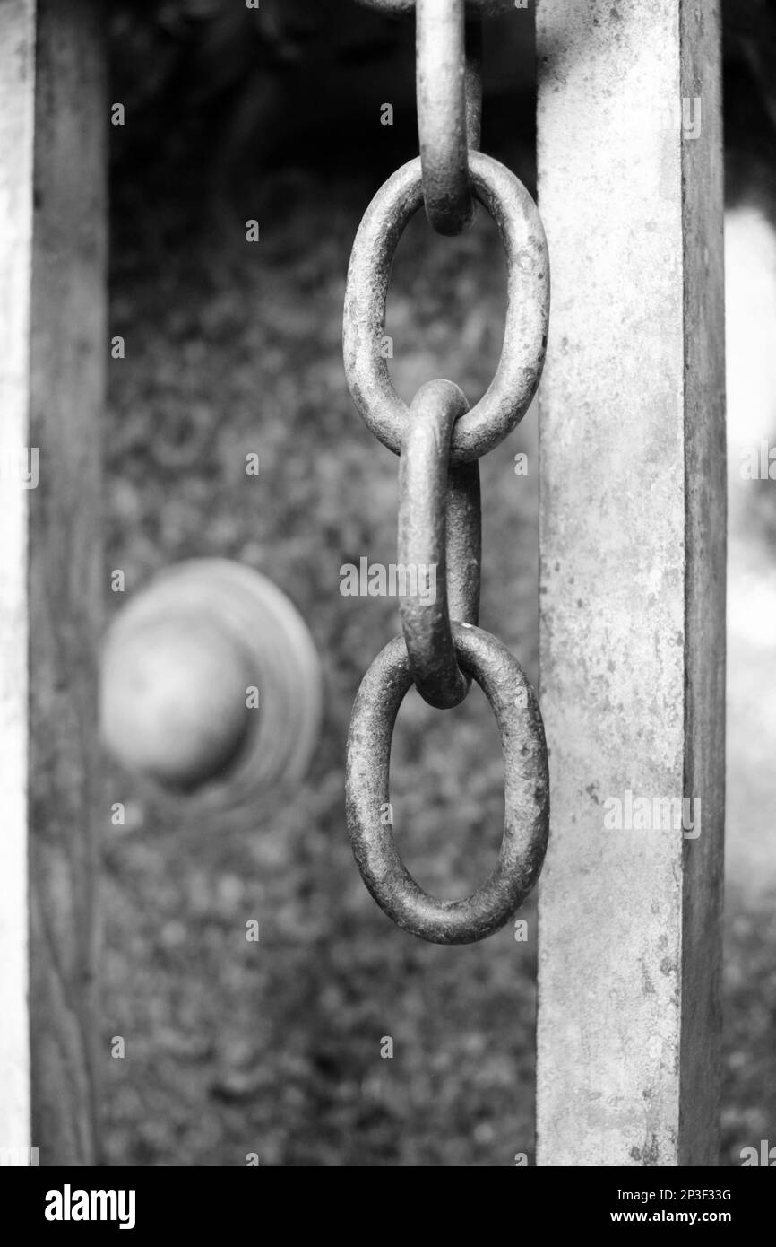 A metal chain hanging from a gate in a black and white monochrome Stock