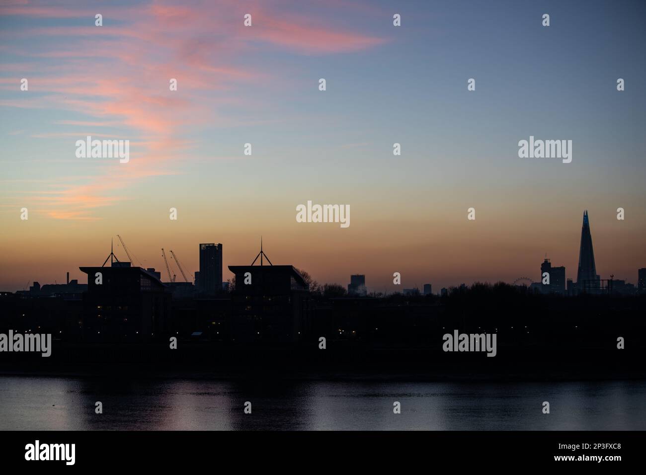 Pink cirrostratus clouds over the river Thames and south east London. The buildings are silhouetted against the sunset sky. Stock Photo