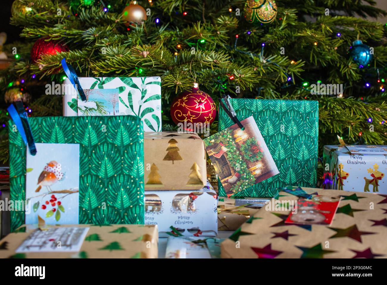 A pile of wrapped Christmas presents lie under the Christmas tree. They're wrapped in different patterned wrapping papers and have gift tags attached. Stock Photo