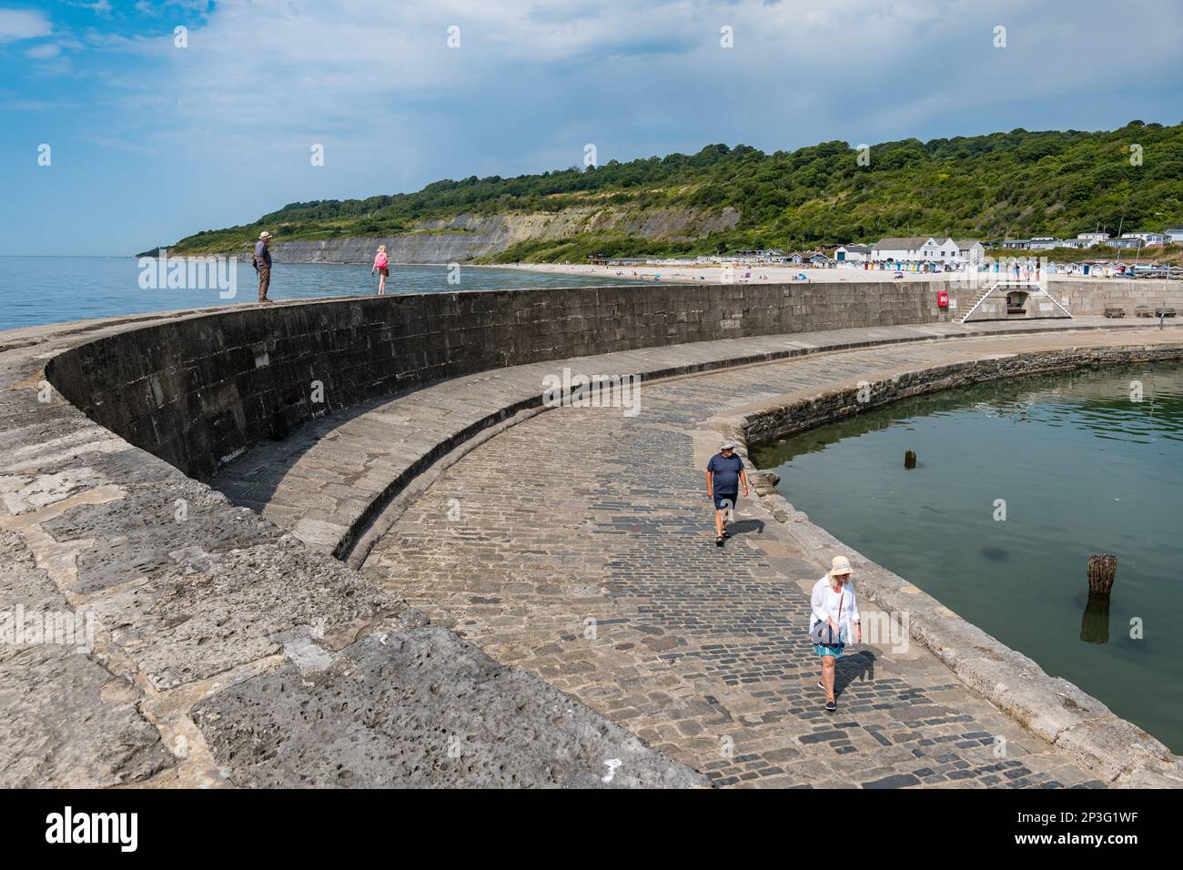 People walking on The Cobb breakwater barrier in Summer heatwave, Lyme Regis, Dorset, England, UK Stock Photo