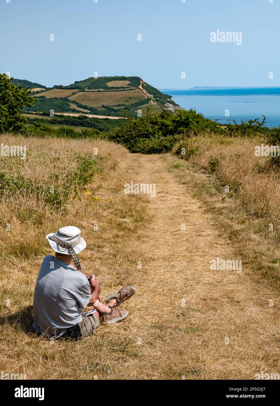 Elderly man resting during Summer heatwave on coastal path, Jurassic coast, Dorset, England, UK Stock Photo