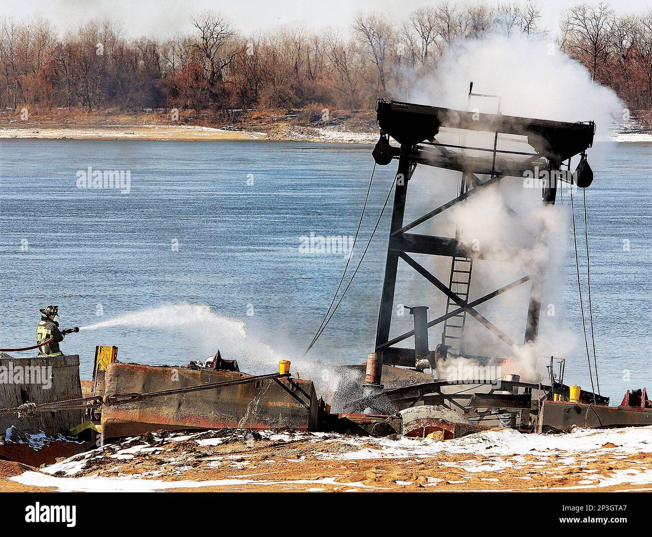 A firefighter sprays water on a half sunken barge burning in the