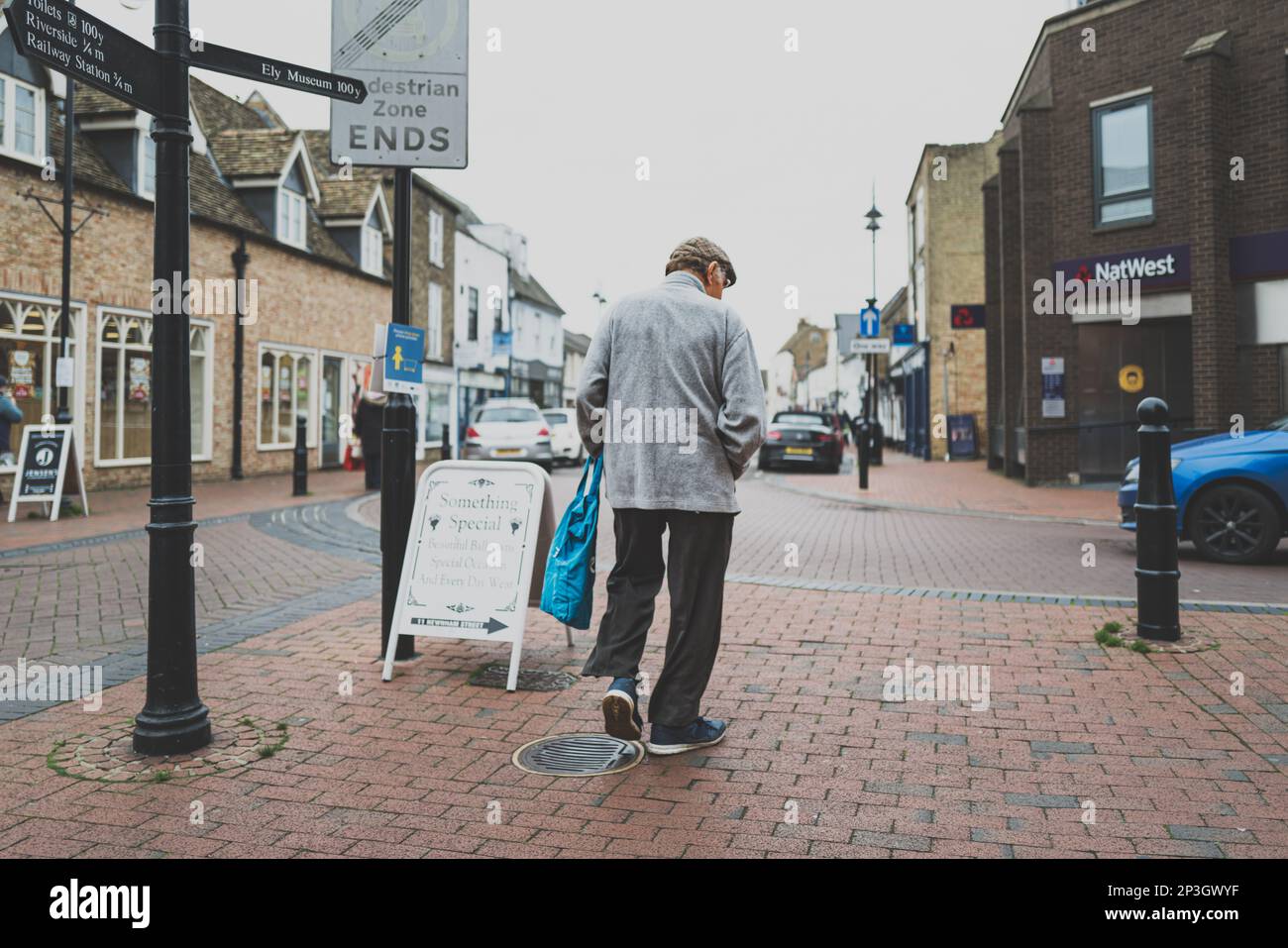 High contrast view of a senior adult man seen walking in a high street setting on a windy day. Stock Photo
