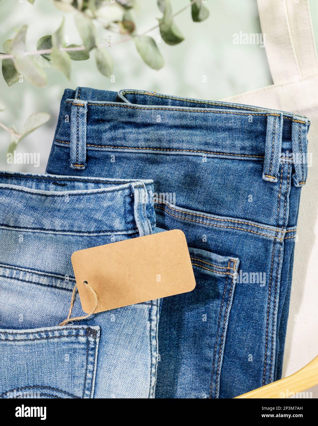 Sustainable still life with jeans with empty craft label, textile bag and hanger. Second hand clothing shop. Casual clothes store, eco friendly sustai Stock Photo