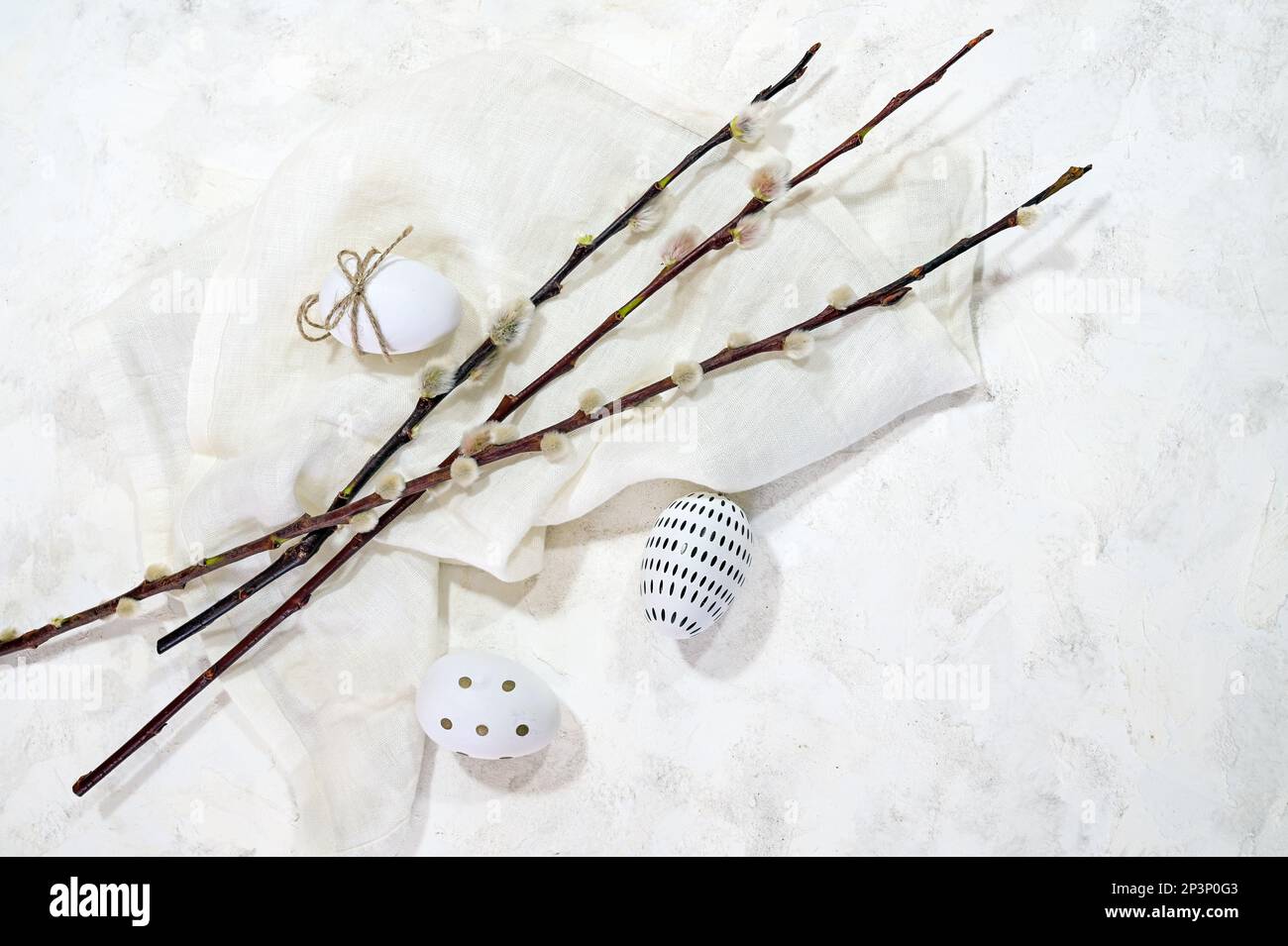 White Easter eggs with small black decor and some willow branches with catkins on a light cloth and background, copy space, high angel view from above Stock Photo