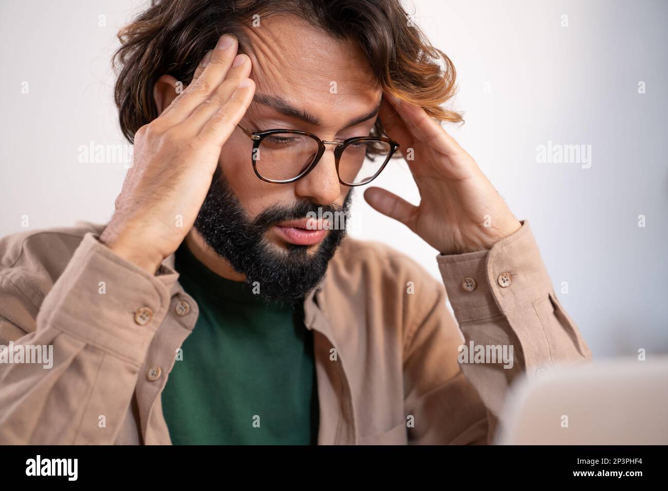 Worried man suffering from headache at work thinking about problems and project deadline. Stock Photo