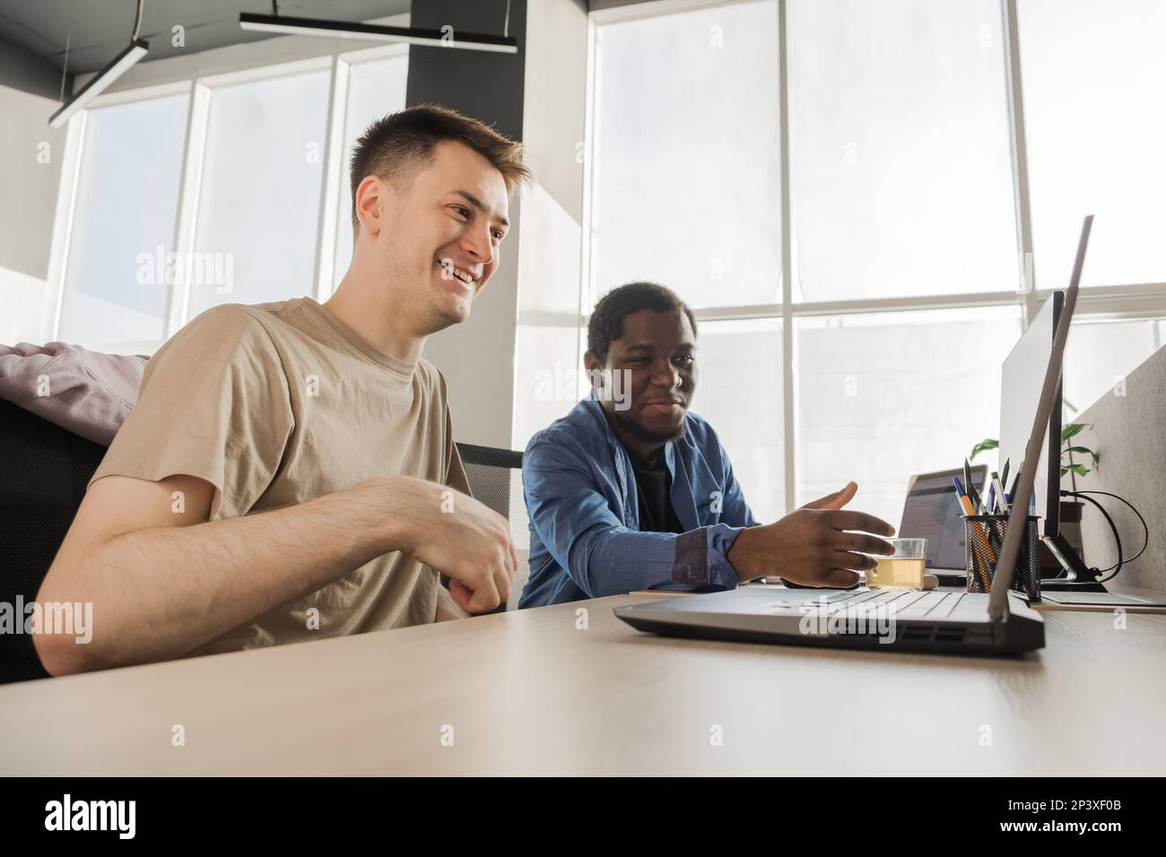 Two smiling positive programmers working in the office of a software development company. Coding technologies, site design. Successful diverse Stock Photo