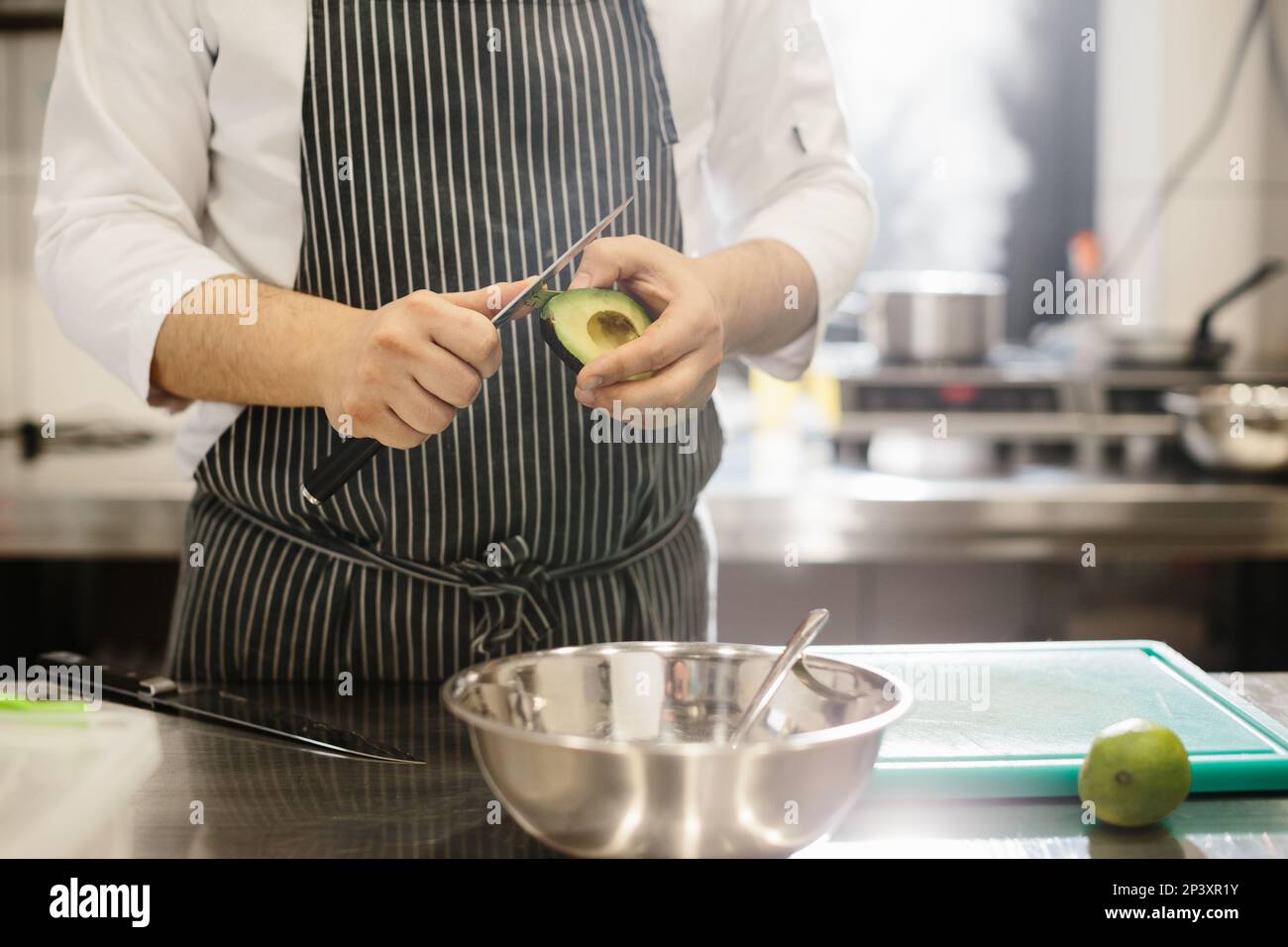 The chef is preparing food. Close-up of a male chef peeling an avocado. Stock Photo