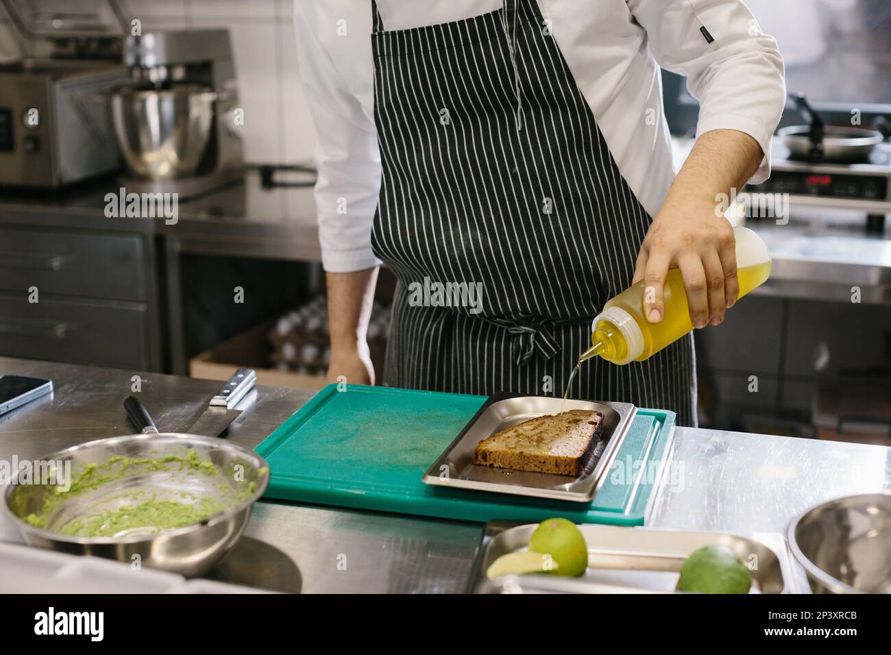 The chef is preparing food. Close-up of a male chef preparing avocado toast in a spacious modern kitchen. Stock Photo