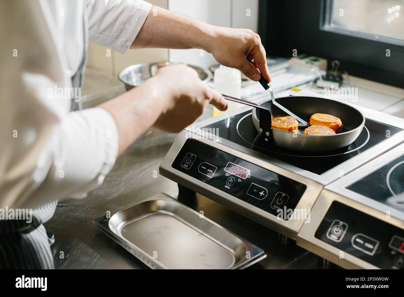 The concept of cooking, professions and people. Male chef frying carrot pancakes in restaurant kitchen. Stock Photo
