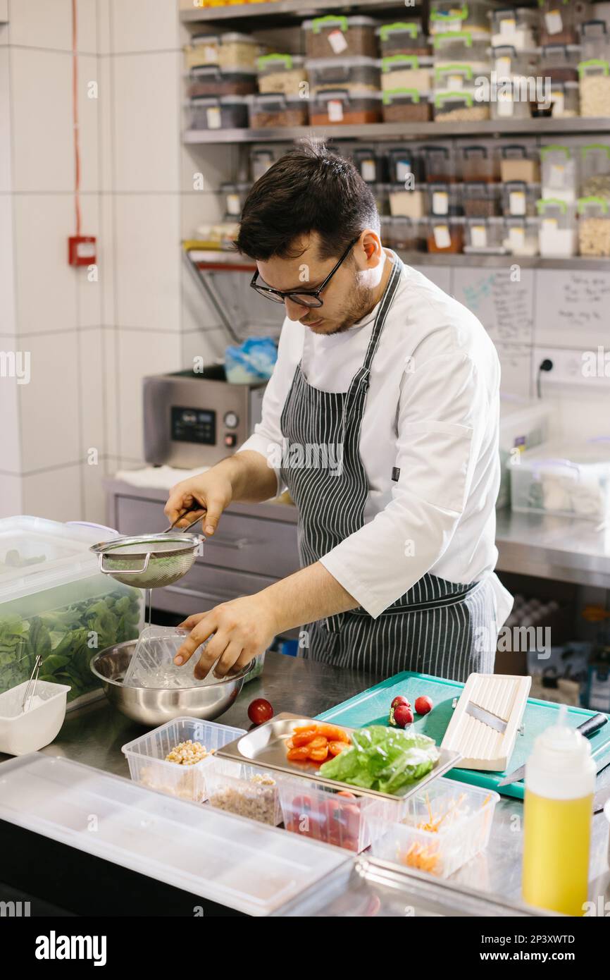 Preparing vegetables for a delicious bowl dish: a male chef in a contemporary restaurant kitchen. Stock Photo