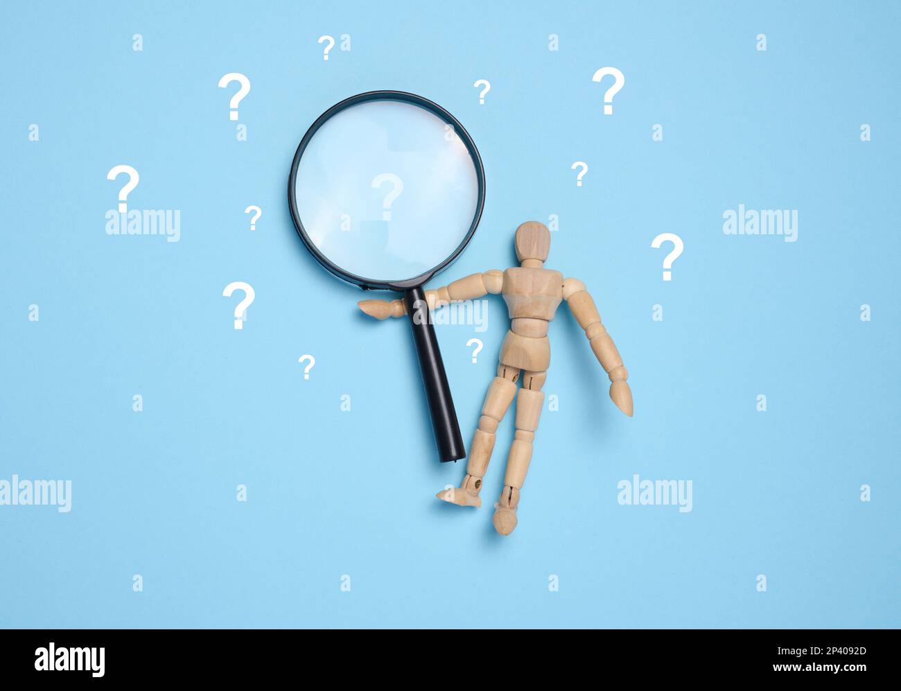 A wooden toy puppet holds a magnifying glass and question marks on a
