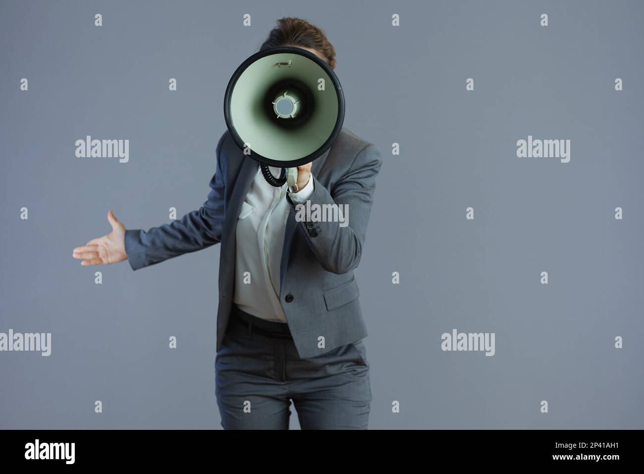 young female employee in grey suit with megaphone isolated on gray. Stock Photo