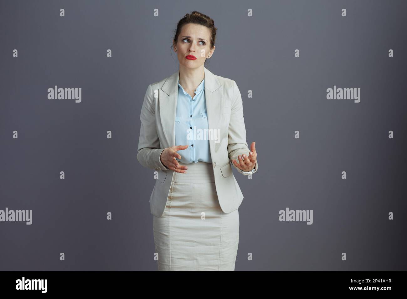 modern woman worker in a light business suit discussing and gesticulating isolated on gray. Stock Photo