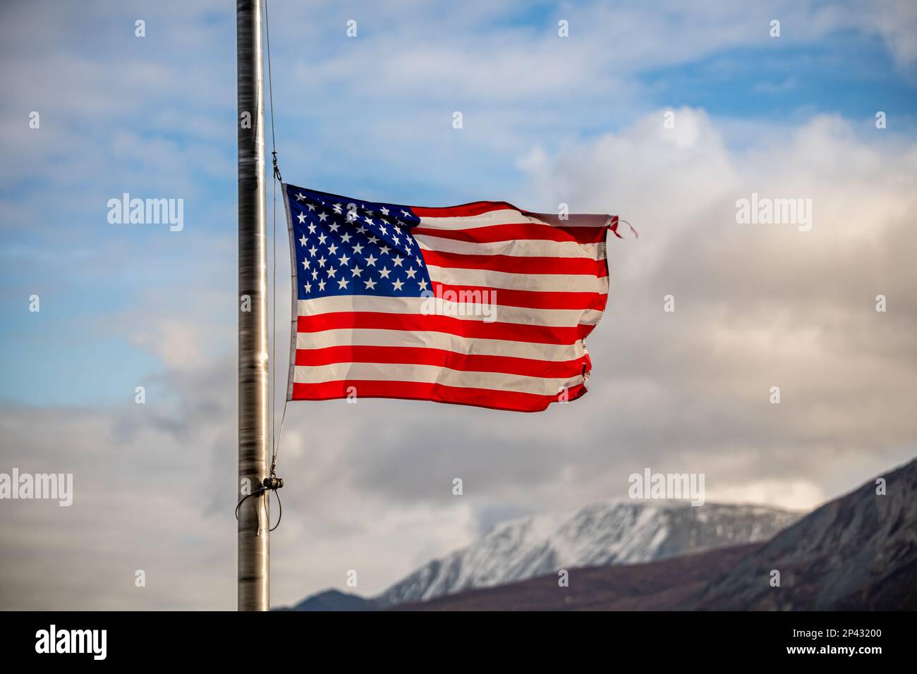 United States of America flag flying half mast with blue sky, clouds
