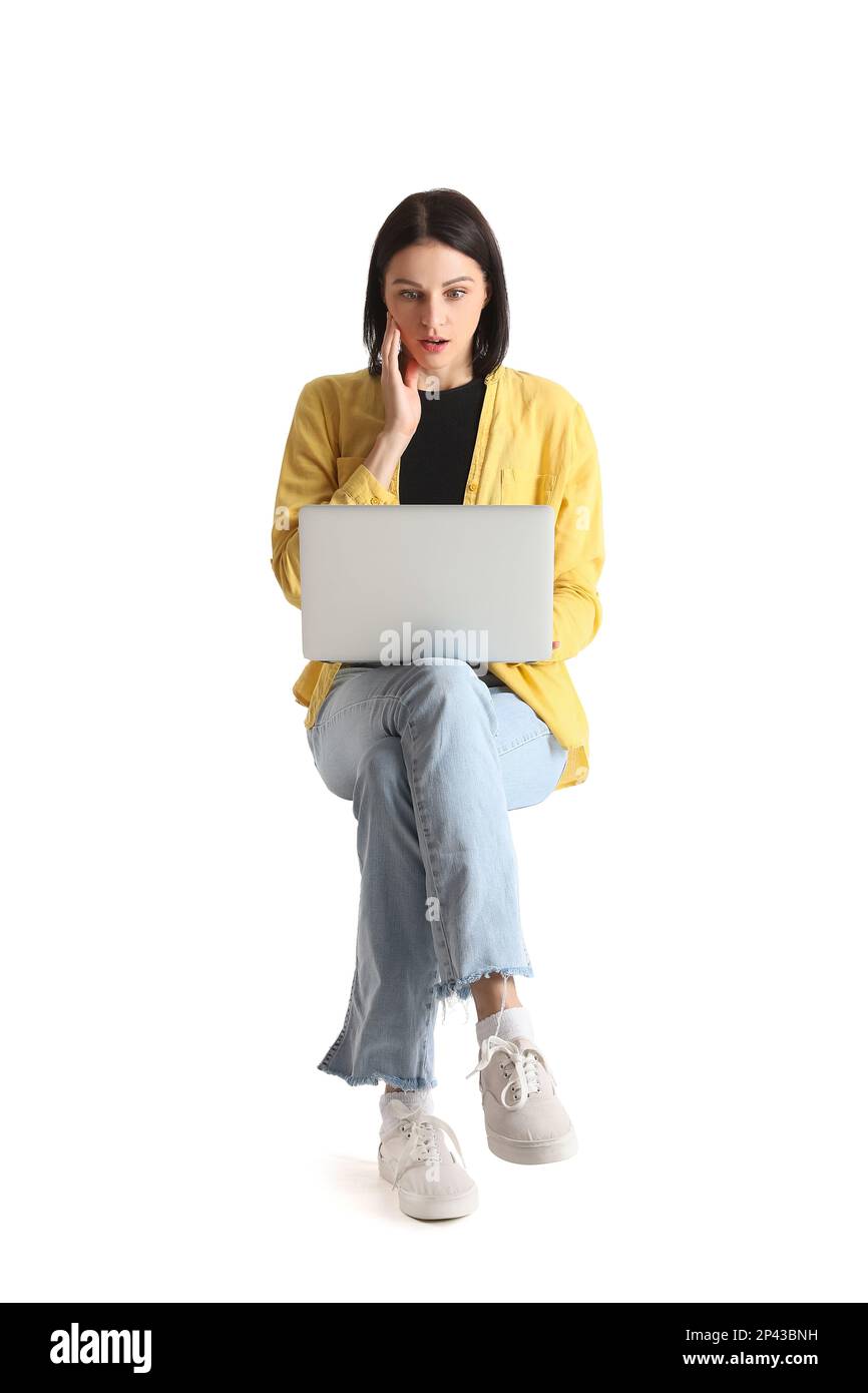 Surprised young woman with laptop sitting on chair against white background Stock Photo