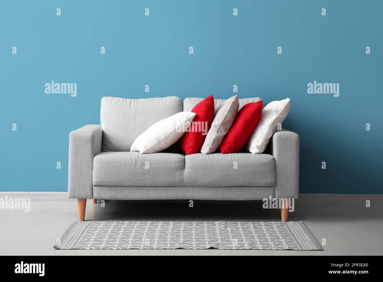 Stylish decorative pillows on cozy grey sofa near blue wall Stock Photo - Alamy