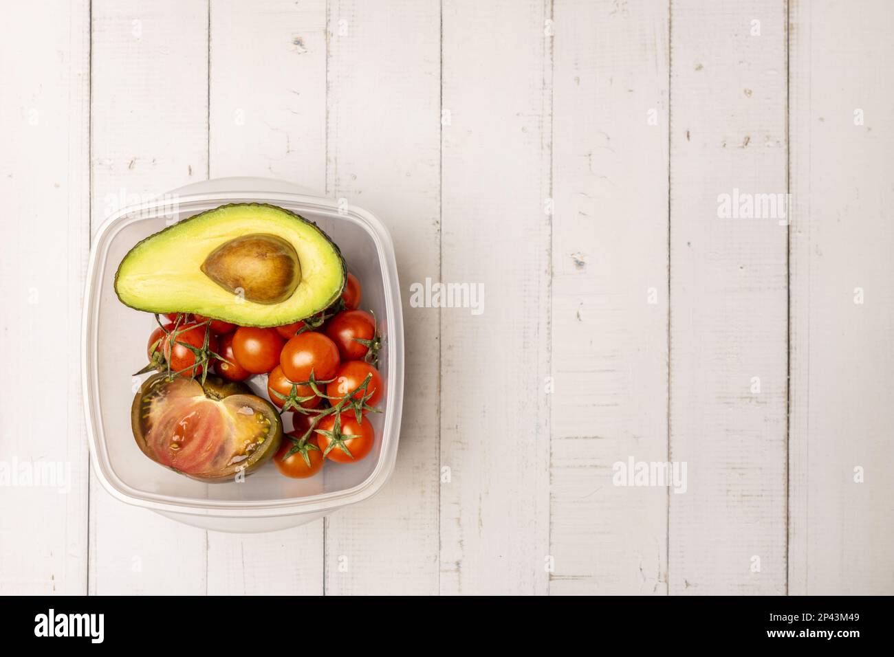 A plastic container for use in the fridge with tomatoes and avocados for salad on a white table Stock Photo
