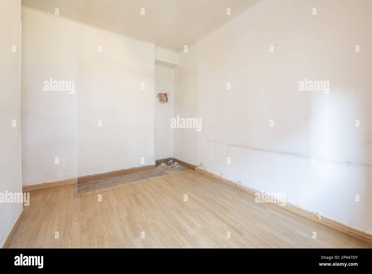 Empty room with poorly installed oak floor, white aluminum window and