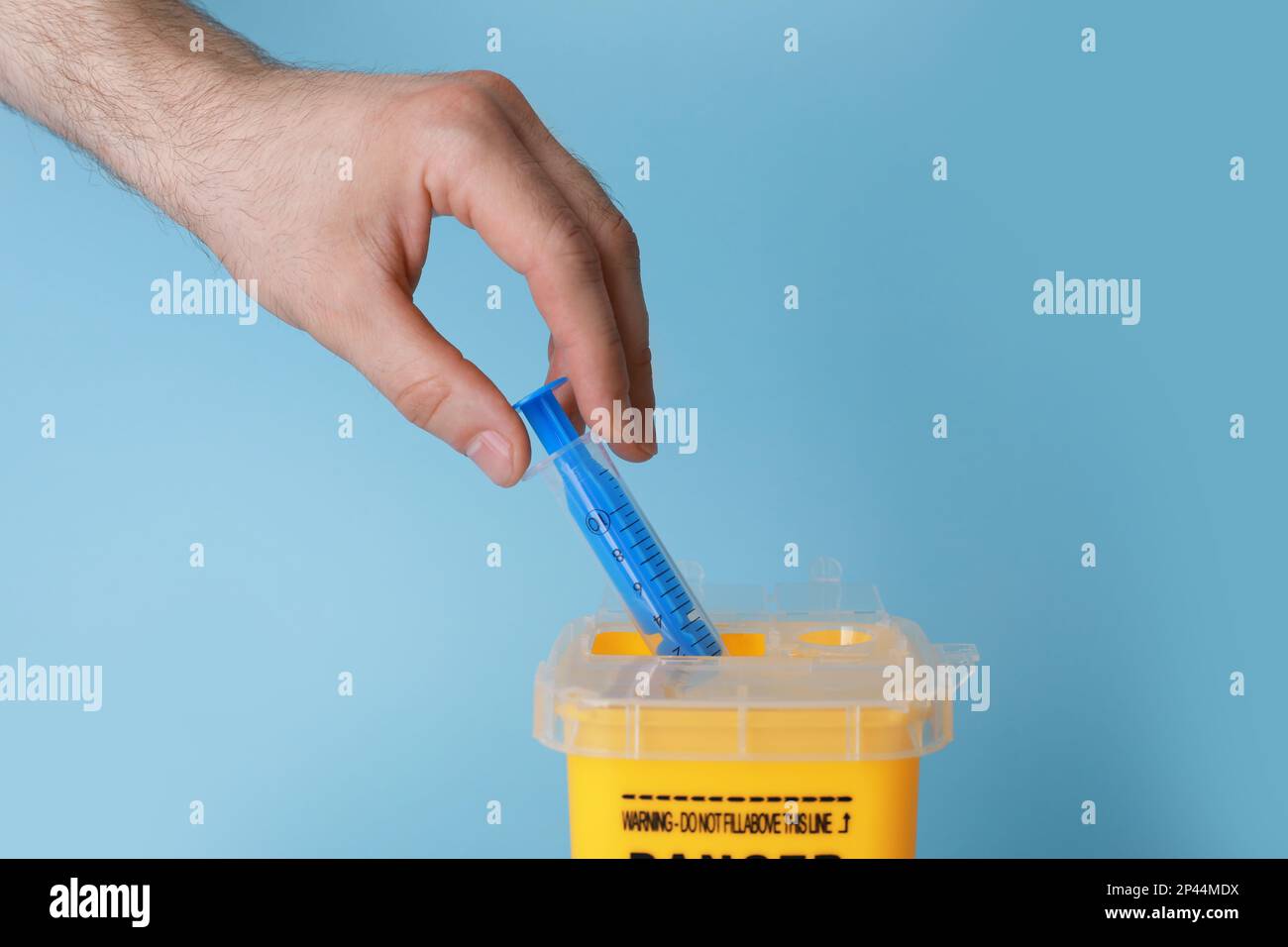 Man throwing used syringe into sharps container on light blue