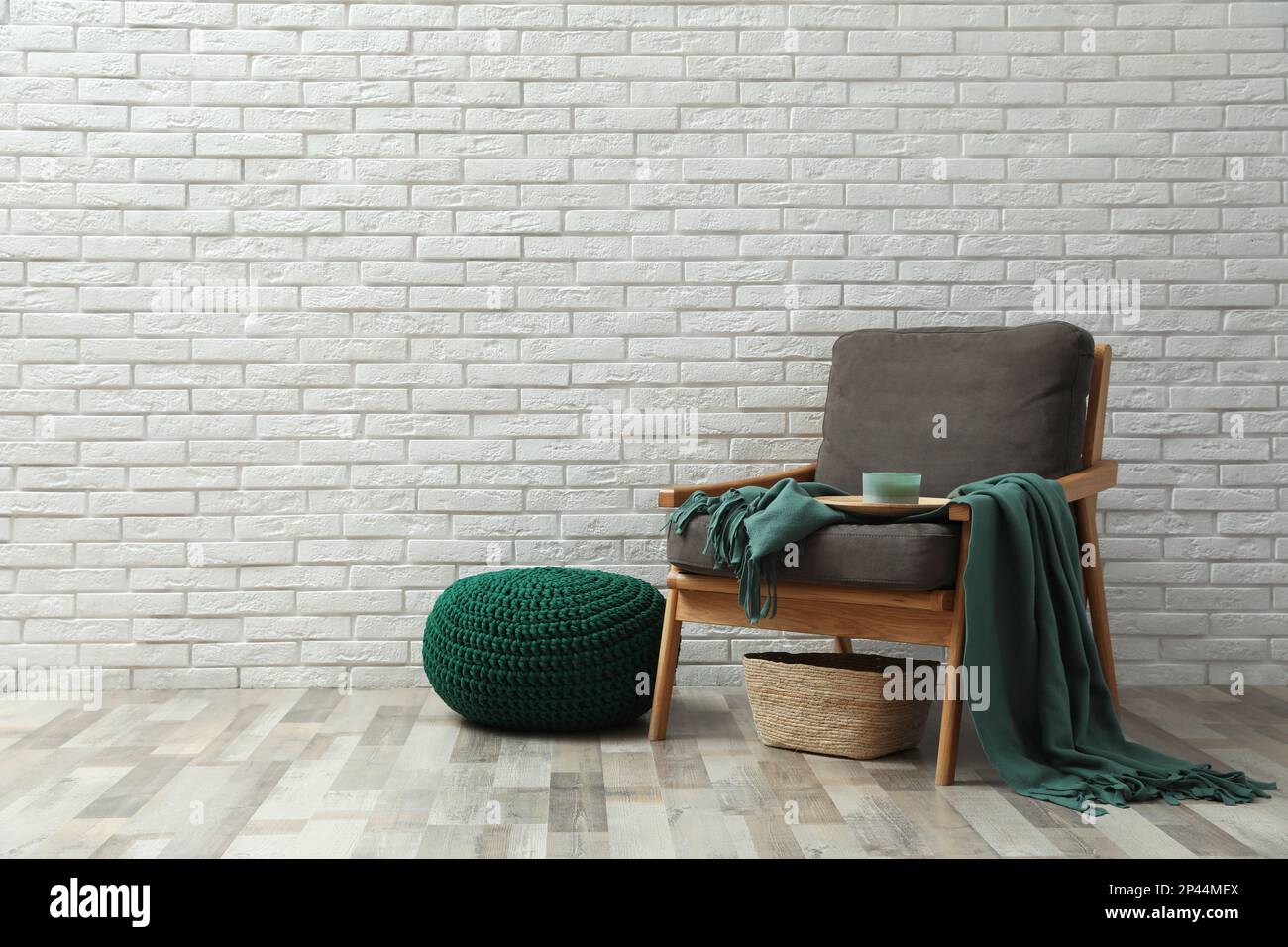 Stylish knitted pouf and comfortable armchair near white brick wall ...