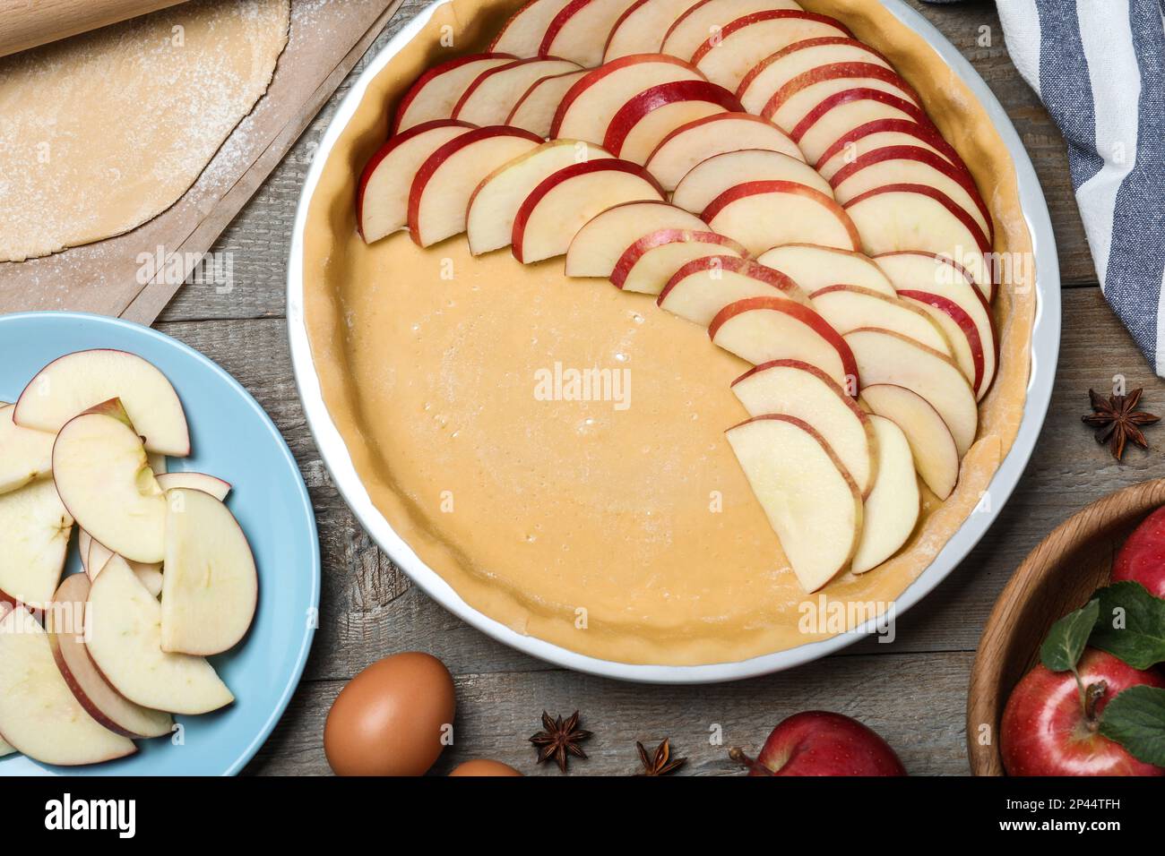 Dish with fresh apple slices and raw dough on wooden table, flat lay. Baking pie Stock Photo