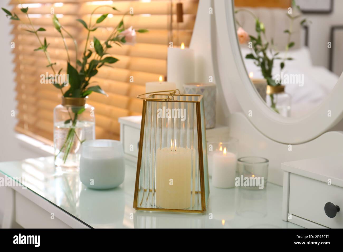 Burning scented candles and bouquet on dressing table indoors Stock
